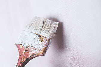 Close-up of a well-used paintbrush with dried paint on a white wall