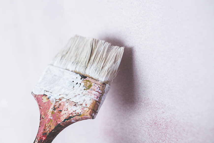 Close-up of a well-used paintbrush with dried paint on a white wall
