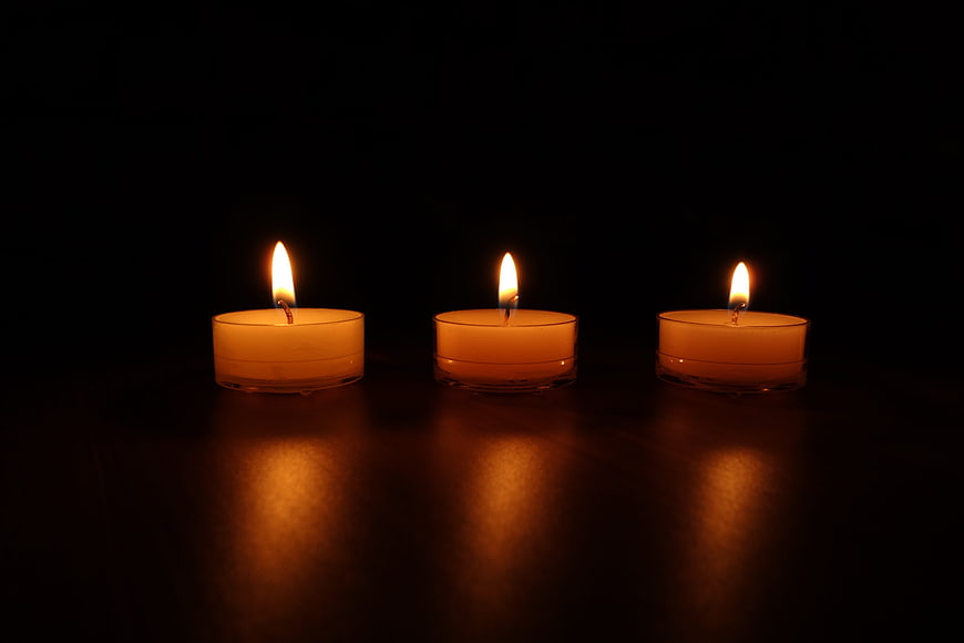 Three lit tea light candles on dark reflective surface