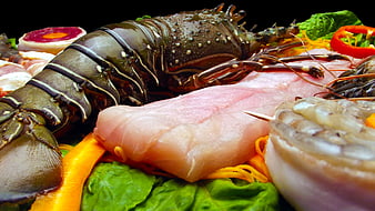 Fresh raw lobster, fish fillet, and shrimp on black background