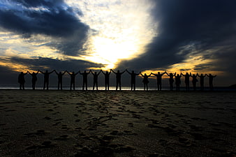 Group of people silhouetted with raised hands on beach at sunset