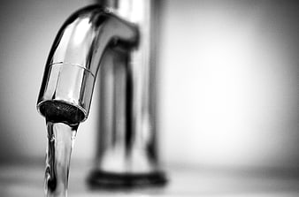 Close-up of water flowing from a chrome faucet in black and white