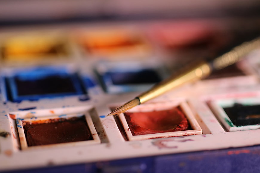 Close-up of paintbrush dipping into red watercolor palette