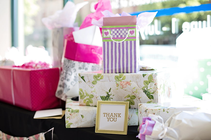 Stack of wrapped gifts with thank you sign on table
