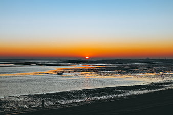 Serene Sunset Over Coastal Mudflats with Distant Boat
