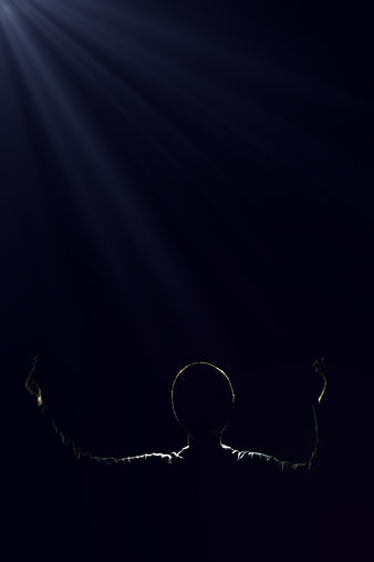 Silhouette of man with raised arms under dramatic spotlight