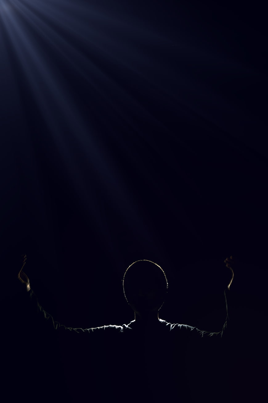 Silhouette of man with raised arms under dramatic spotlight