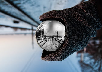 Hand holding reflective crystal ball with train tracks reflection