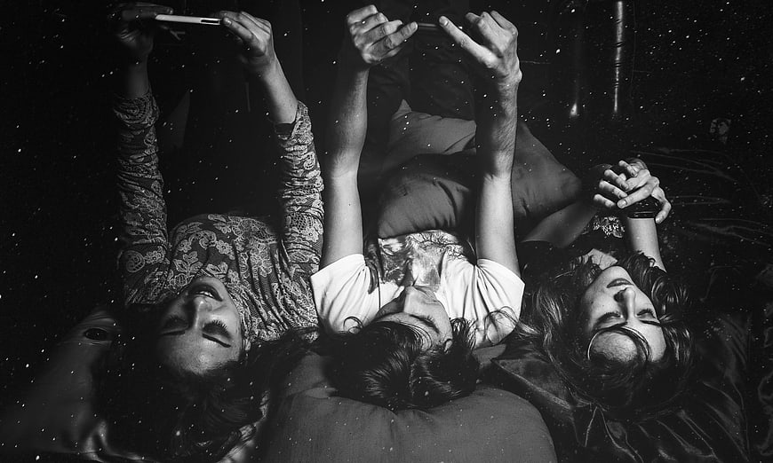 Three women lying down looking at smartphones in black and white