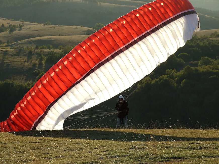 Paraglider Pilot Preparing for Takeoff on Grassy Hill
