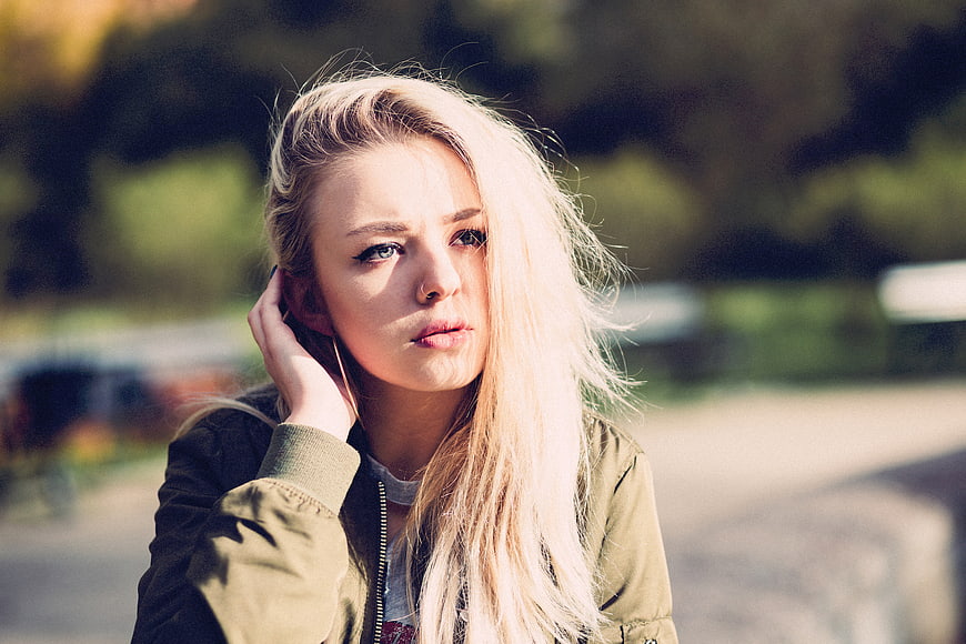 Blonde Woman in Olive Jacket Looking at Camera Outdoors