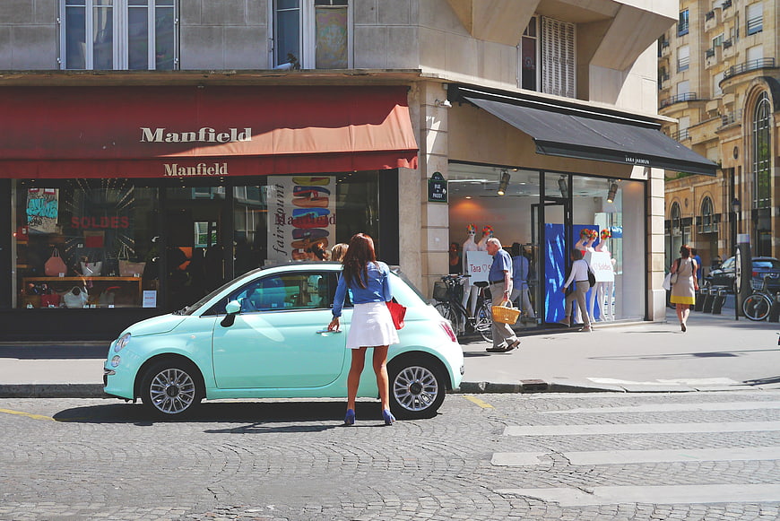 Woman in White Skirt Standing by Mint Green Car on City Street