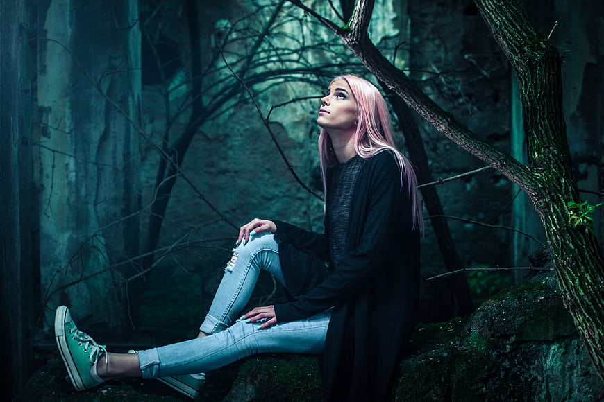 Pink-haired woman sitting in dark moody forest ruins