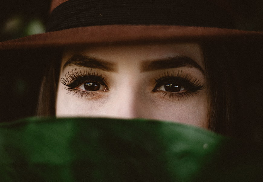 Close-up of woman's eyes with hat and green leaf