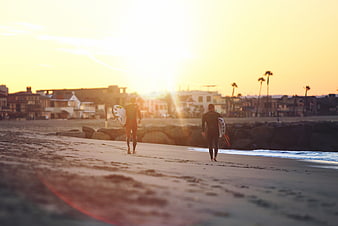 Surfers walking on beach at sunset with surfboards