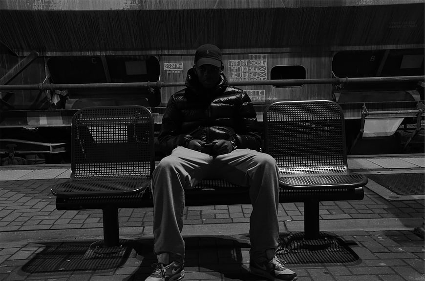 Man Sitting on Bench at Train Station in Black and White