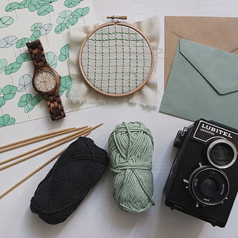 Flat lay of knitting supplies, vintage camera, and wooden watch