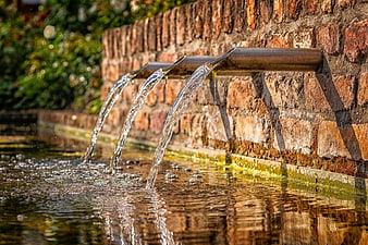 Water Flowing From Metal Spouts Into A Brick Fountain
