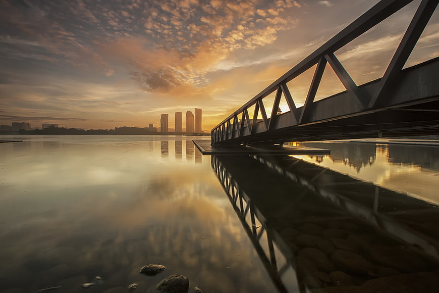 Sunset Reflection on Calm Water with Steel Bridge and City Skyline