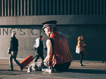 Man in red vest and hat sitting on urban ledge