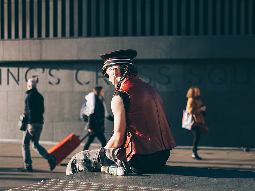 Man in red vest and hat sitting on urban ledge