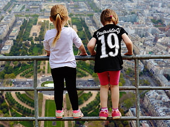 Two young girls standing on railing overlooking Paris cityscape