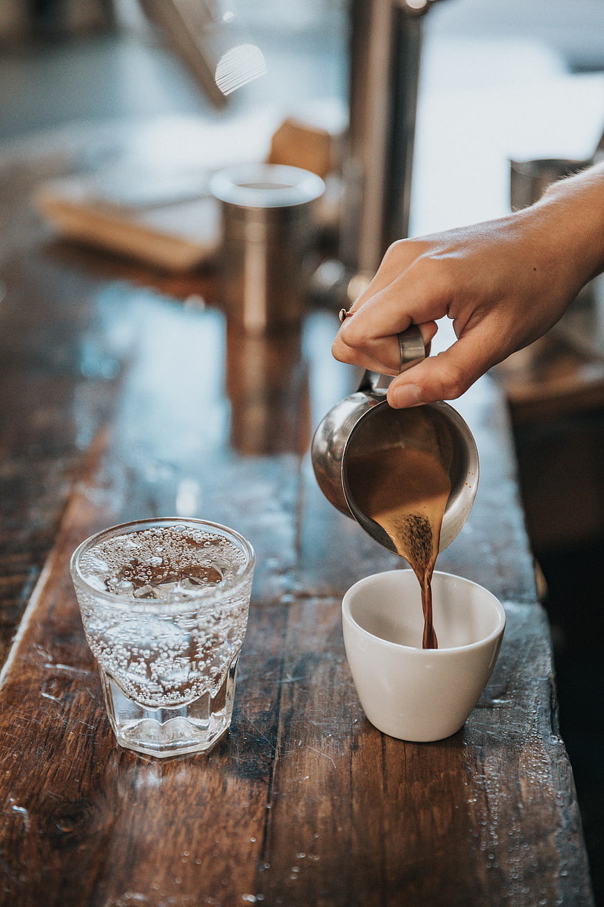 Barista pouring espresso into a white cup on a wooden table