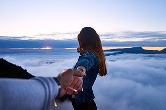 Couple holding hands overlooking sea of clouds at sunrise