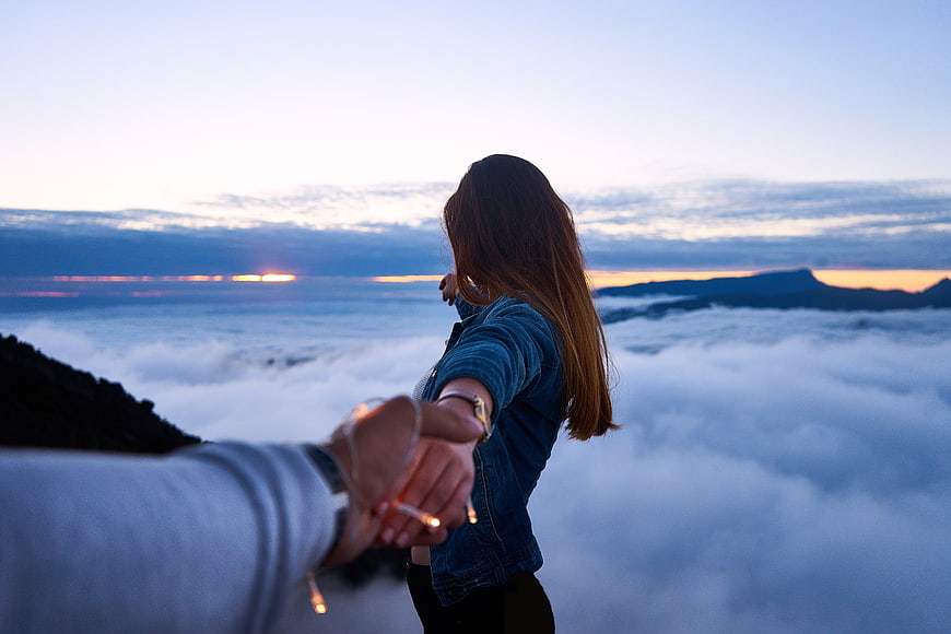 Couple holding hands overlooking sea of clouds at sunrise