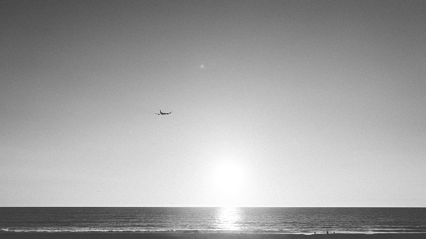 Airplane Flying Over Ocean at Sunset Black and White