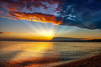 Dramatic sunset over calm sea with sunbeams breaking through clouds