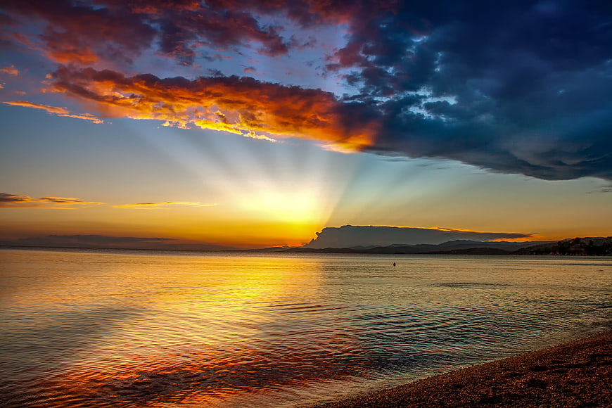 Dramatic sunset over calm sea with sunbeams breaking through clouds
