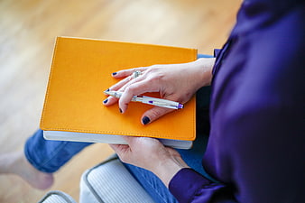 Woman holding orange notebook and pen on lap
