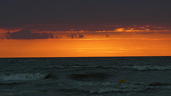 Dramatic orange sunset over dark ocean waves