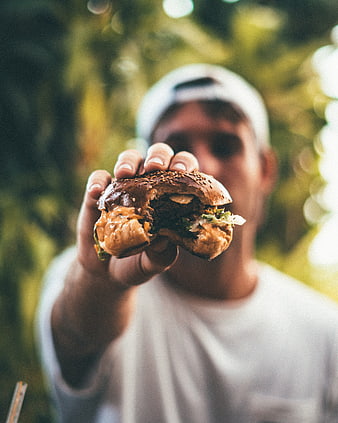Man holding juicy burger towards camera outdoors