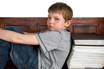 Discouraged young boy sitting next to a large stack of homework books