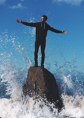Man standing on rock with arms outstretched amidst crashing waves