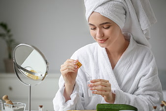 Woman in white robe applying serum with dropper