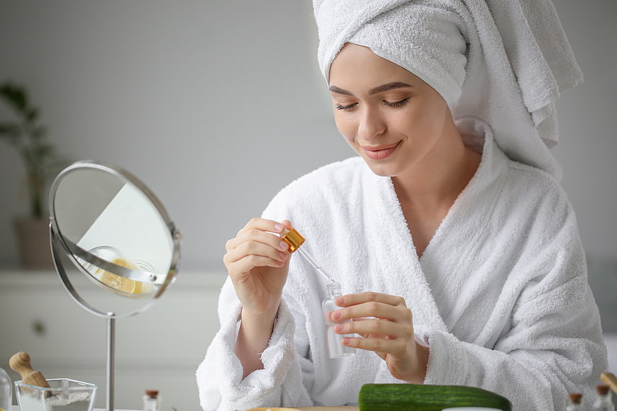 Woman in white robe applying serum with dropper