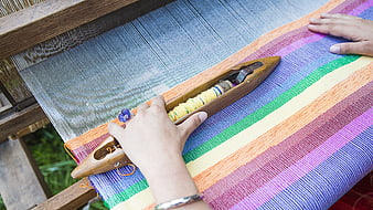 Hands weaving colorful striped textile on traditional wooden loom