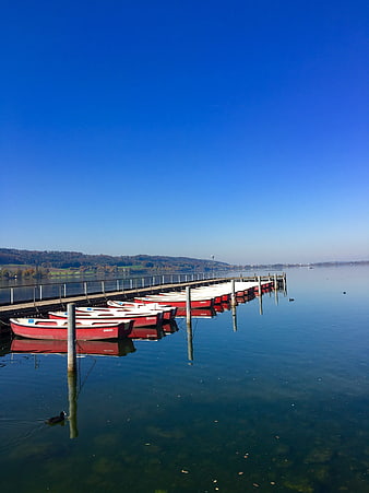 Red rowboats docked on a calm lake with blue sky