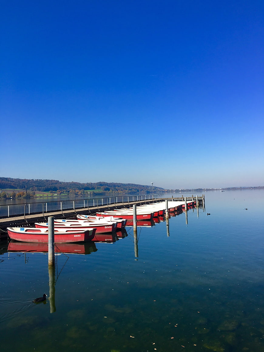 Red rowboats docked on a calm lake with blue sky