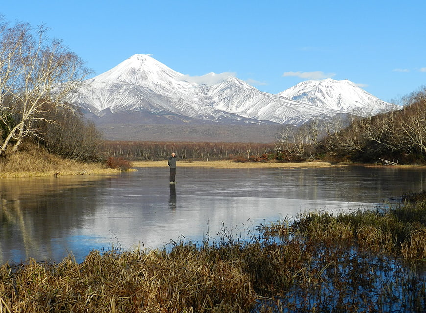 Lone figure standing on frozen lake with snow-capped mountains