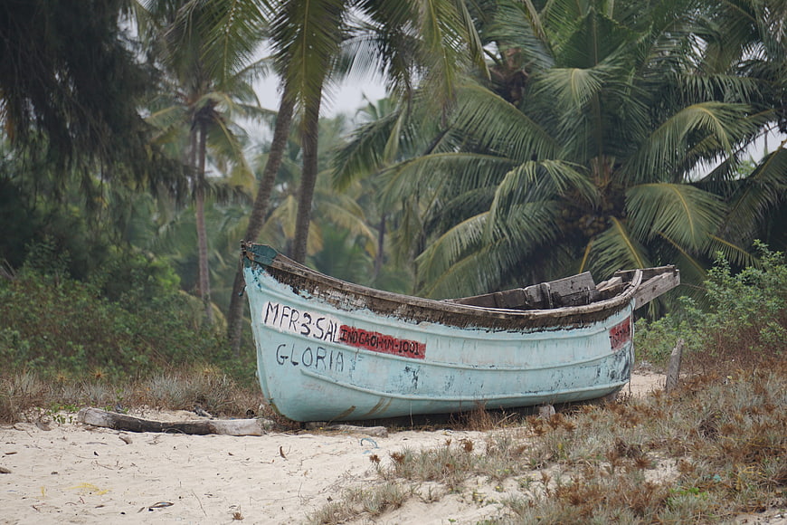 Weathered fishing boat on tropical beach with palm trees
