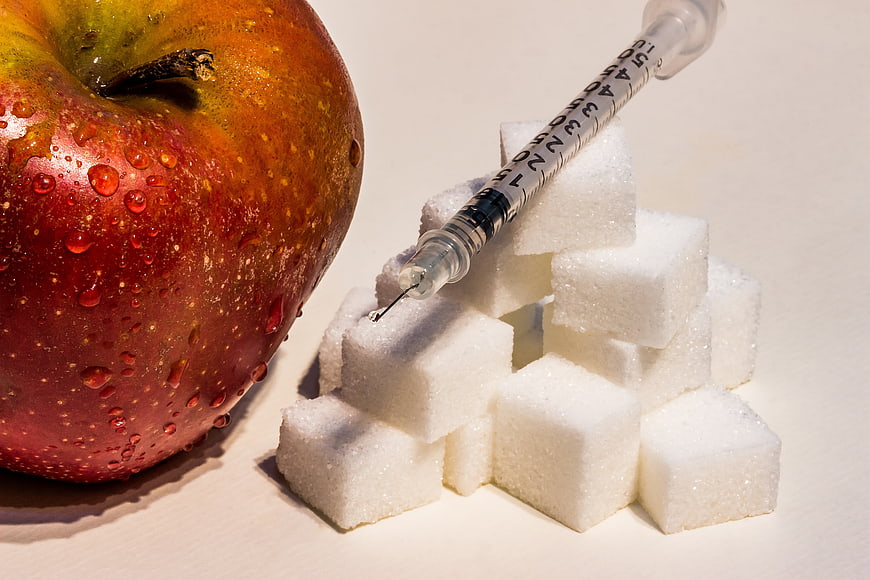 Insulin Syringe Resting On Sugar Cubes Next To A Wet Red Apple