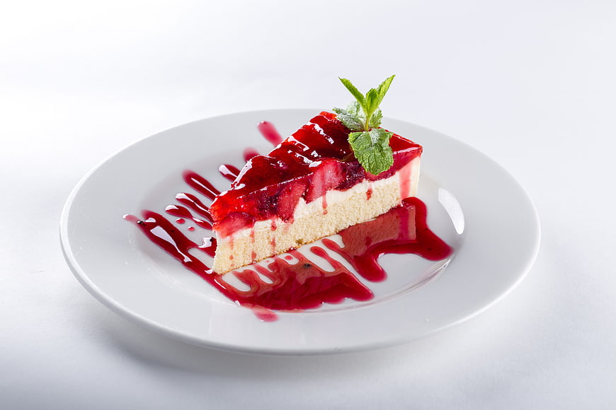 Strawberry cheesecake slice with berry sauce on white plate