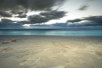 Dramatic cloudy sky over calm turquoise beach with footprints