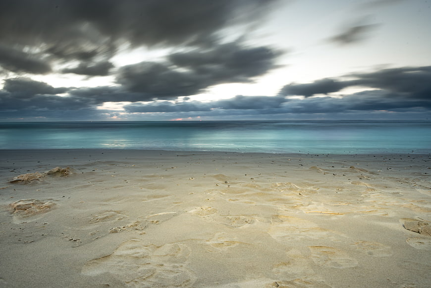 Dramatic cloudy sky over calm turquoise beach with footprints
