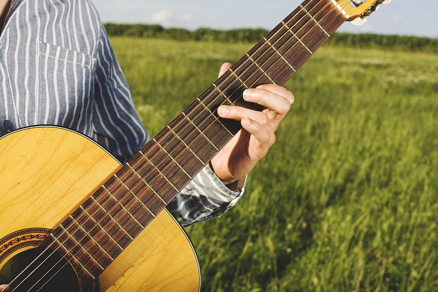 Close-up of hands playing acoustic guitar in a green field