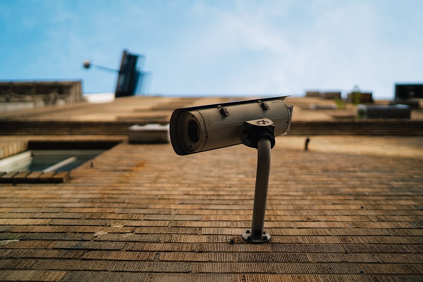 Weathered Security Camera On Rooftop With Blurred Urban Background